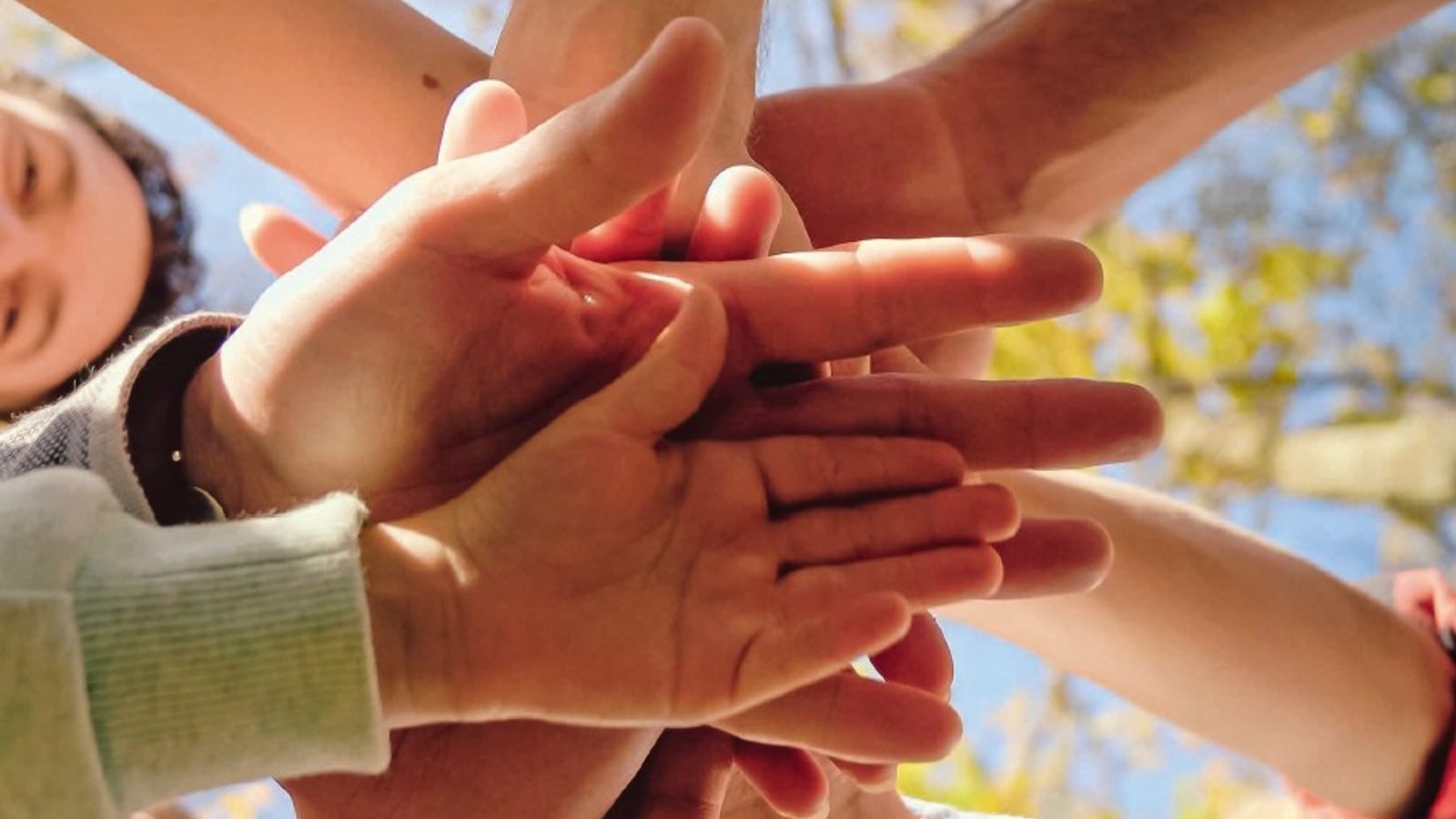 Eine Gruppe von Menschen steht im Kreis und streckt ihre Hände in die Mitte. Diese Geste vermittelt ein Gefühl von Gemeinschaft, Zusammenhalt und Unterstützung.